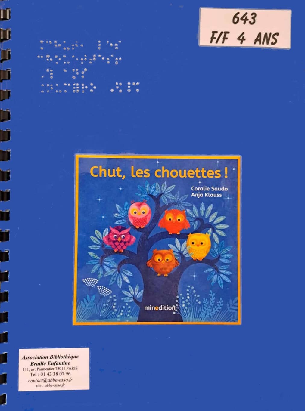 Une couverture bleue intitulée « Chut, les chouettes ! » représente cinq hiboux colorés perchés sur un arbre. La couverture est ornée de texte en braille, d'autocollants de bibliothèque et d'une reliure spirale à gauche.